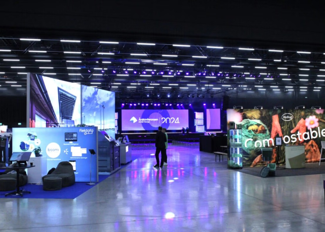 A photo from Sirk Norge Annual Conference with booths around and bright lights from the booths illuminating on the floor.