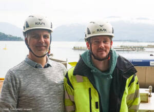 A photo of 2 men wearing helmets with aquaculture net circles in the background.