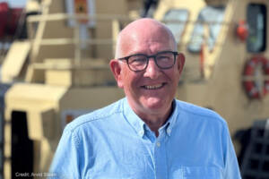 A photo of a man (Ole Arthur Vaage) smiling for the camera on a sunny day with a ship in the background.